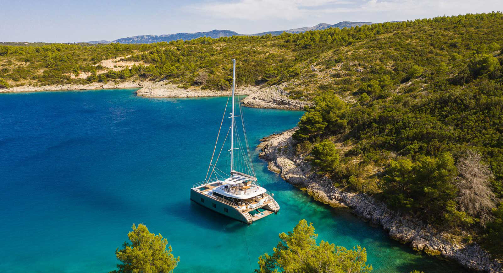 Electric, solar-powered catamaran, the Sunreef 60 Eco, anchored on a bay surrounded by green hills.